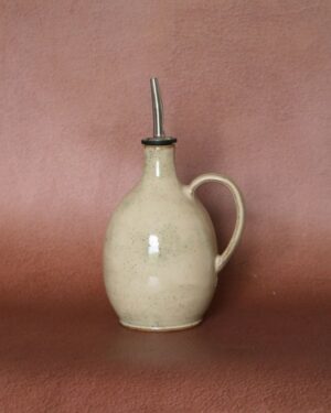 Huilier en céramique artisanale beige moucheté avec anse et bec verseur en inox, vue de face.