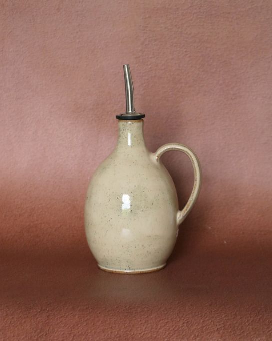 Huilier en céramique artisanale beige moucheté avec anse et bec verseur en inox, vue de face.