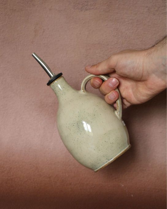 Bouteille à huile en grès fait main dans la Loire tenue par une main pour montrer sa taille.