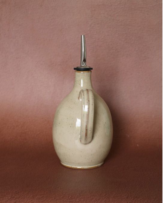 Détail de l'anse ergonomique d'un huilier en poterie artisanale crème et mouchetée.